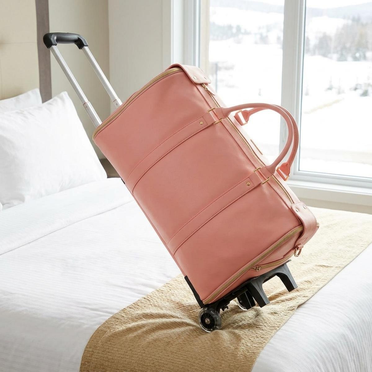 The rose pink Luhxe Travel Bag 2.0 packed and zipped on a hotel bed